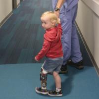A doctor, who is out of frame, holds Arlo’s hand as they walk together down a hallway.