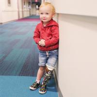Arlo Yost leans against the wall of a hallway and smiles for the camera, with his prosthetic proudly visible.