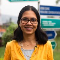 Dr. Shenoi smiles in front of a signpost outside.