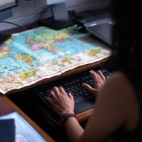 Dr. Shenoi types on her computer with a world map on her desk in front of her.
