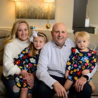 Dr. Adkins and his wife and two little girls smile for a family photo on the couch.