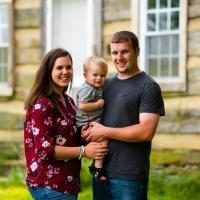 A family photo of Caleb, Amelia, and Cason in front of Caleb's family cabin.