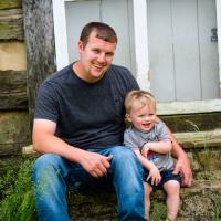 Caleb and his young song Cason sit and smile together on some steps for a photo outside.