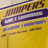 A yellow and purple banner reading “Jumpers Girls Swimming - Regional Champions - 2010 - Callie Garner - 50 Free”