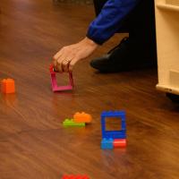 A close-up photo of a Child Life team member’s hand picking up a LEGO off the floor.
