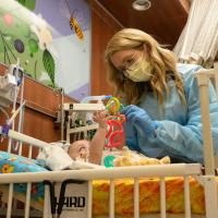 A photo of Ashlee holding a colorful children’s toy above a young patient in a crib.