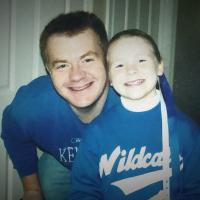 A family photo of a young Christa and her father smiling at home in their UK gear. He is a young white man with short ginger hair, and he is wearing a University of Kentucky sweater.