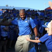 Courtney walks through a crowd of fans, all wearing blue, before a football game. He holds his arm out to give a kid a high five.