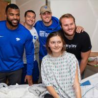 Courtney and three other football players pose with a Kentucky Children’s Hospital patient. The patient, a young girl, is sitting in her bed and wearing a hospital gown.