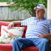 Danny sits out on the porch in a blue and white striped shirt with a white and blue UK cap.