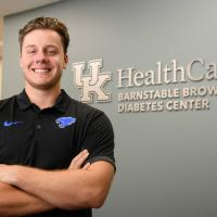 Dillon smiles in front of the UK HealthCare Barnstable Brown Diabetes Center sign in a hallway.