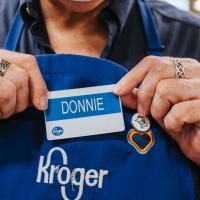 Donald holding his name badge, which says “Donnie” and is attached to his Kroger employee apron, in front of his chest.