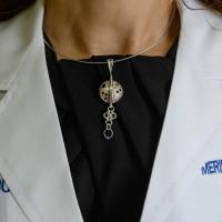 A close-up of a necklace that has a circular pendant with holes representing the brain, and a piece of other circles attached to it.