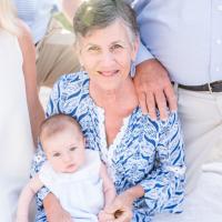 An older photo of E, with short grey hair, holding her grandchild and surrounded by family members.