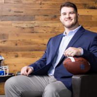 A photo of Eli smiling as he poses in an armchair with a football and his helmet.