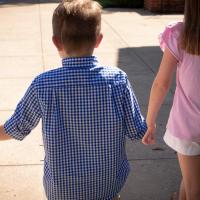 A photo from behind Elliott as he walks in between his mother and sister holding both of their hands.