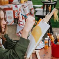 Evan is painting different colours, yellow and orange, on a canvas in an outside setting.
