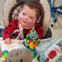 A photo of Everett sitting in his high chair and smiling. His trach tube can be seen connected to his throat.