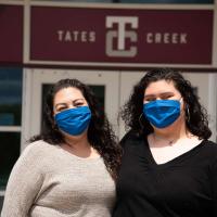Faith and her mom wear blue face masks and smile in front of the Tates Creek high school front doors.