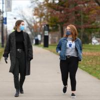 Fielden and another college student smile at each other as they walk down a path on UK’s campus. Both are wearing masks.
