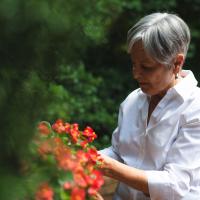 Gayle tends to a plant with red blossoms out in her garden.