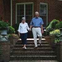 Gayle and her husband hold hands and walk down their front steps.