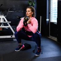 Geri looks focused as she squats holding a kettlebell while working out in the gym.