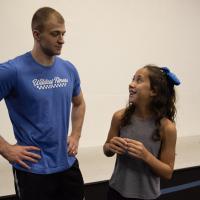 Gracie pictured with a young adult male in a gymnasium after practicing cheerleading stunts. She is looking up at him and smiling.