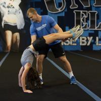 Gracie, a high school age girl with brown hair, practicing a back handspring with the help of a tall young adult male.