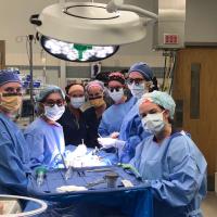 An all-female pediatric endocrinology team, all dressed in blue scrubs and surgical headgear with masks, circled around an operating table.
