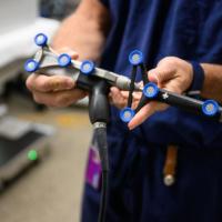 A close-up photo of the robotics system that assisted Dr. Selby during Helen’s surgery. It is a black and gray apparatus with a long needle at the end, and blue discs used for gripping and positing that span the distance of the machine.