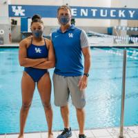 Jaida poses for a photo on the side of the pool with her coach, Ted Hautau, a middle aged man with blonde hair wearing a blue University of Kentucky polo and khaki shorts. Both are wearing masks.