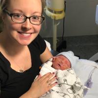 Jennifer smiles as she holds a newborn Jeremiah, who is swaddled in a blanket.