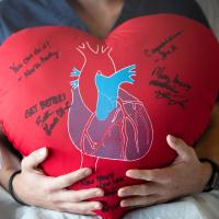 A large, red, plush heart with an anatomical heart printed in the front is signed in sharpie by members of the patient's care team at the hospital.