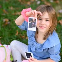 A close-up photo of Kailey sitting in the grass and holding up a polaroid picture of her dancing.