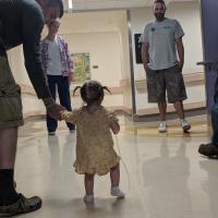 A candid photo of Max holding young Kailey’s hand as they walk down the hospital hallway with several people looking on.