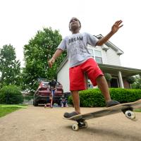 A candid photo of Malakai riding a skateboard in his driveway.