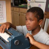 A photo of Malakai sitting at home and practicing on his typewriter.