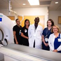 Margie stands and smiles for a photo with a group of nurses next to a CT scanning machine.