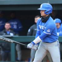 Marshall on a baseball field in his blue UK baseball uniform with a bat, ready to swing.