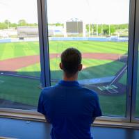 A photo of Matt from behind as he looks over the field from a box seat.