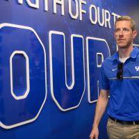 A candid of Matt walking through a hallway that has a large UK Athletics branded decal on the wall.
