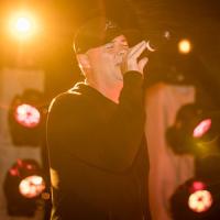 A photo of Coach Mitchell singing into a microphone while on stage. Colorful stage lights can be seen behind him.