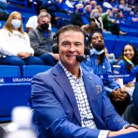 A photo of Coach Mitchell smiling as he looks off camera while sitting courtside at a UK game.