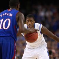 An action shot of Michael playing defense while a Kansas basketball player dribbles the ball.