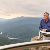 A landscape photo of Michael at an overlook, looking out across a view of the sky, mountains and trees.
