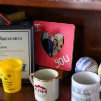 A close-up photo of a shelf featuring a framed picture of Michael and his daughter, mugs, baseballs and a certificate of appreciation.