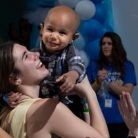 A photo of a young woman holding up a smiling baby at a DanceBlue event.