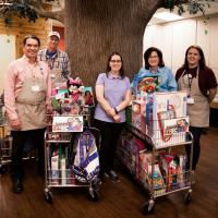 A photo of Doug, Claire, Jennifer, and two volunteers smiling and posing in front of toys for Jarrett’s Joy Cart.