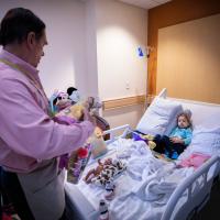 A candid shot of Doug delivering a doll from Jarrett’s Joy Cart to a sick young girl in a hospital bed.